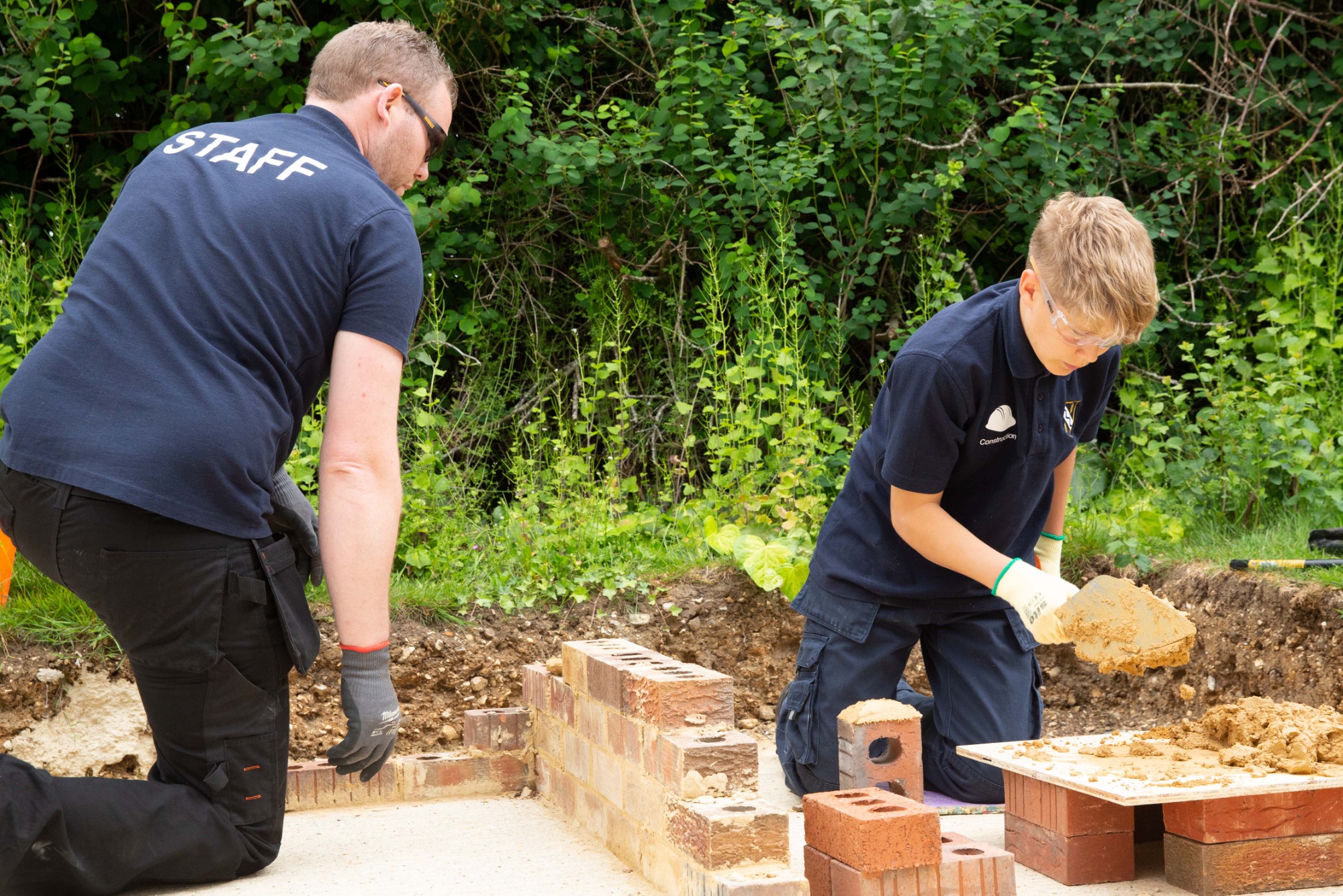 Kennet School student practicing bricklaying under teacher supervision.